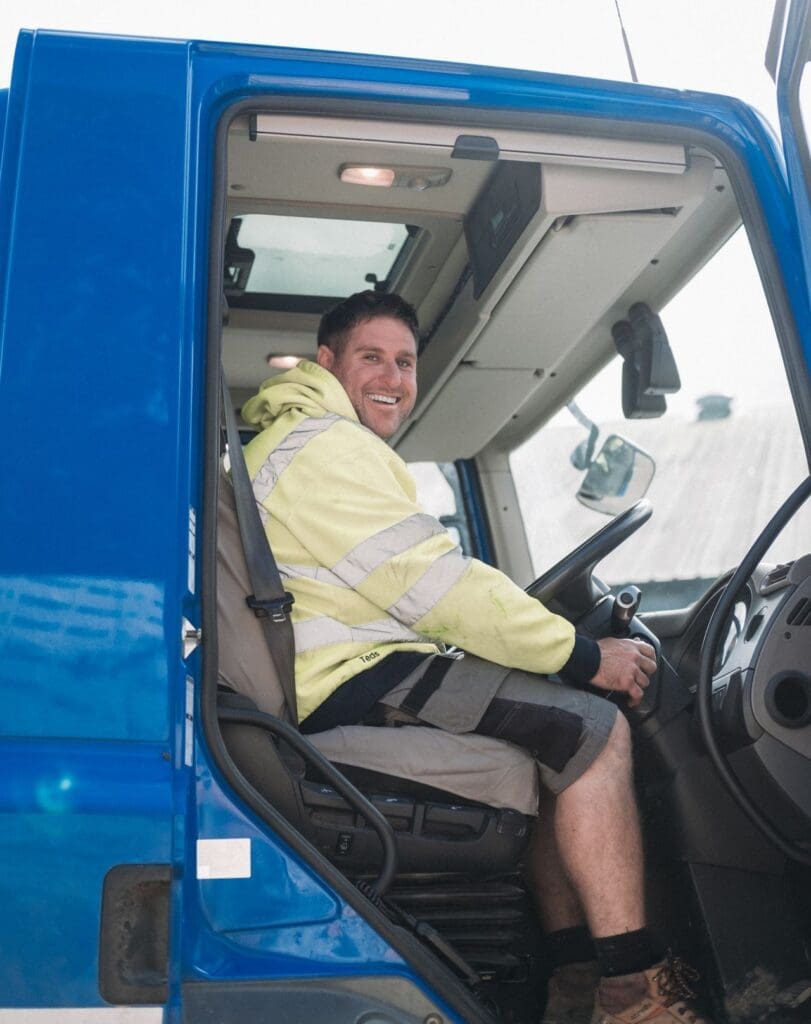 Jamie Arnold, timber frame delivery driver, smiling from the cab of a Sydenhams delivery vehicle