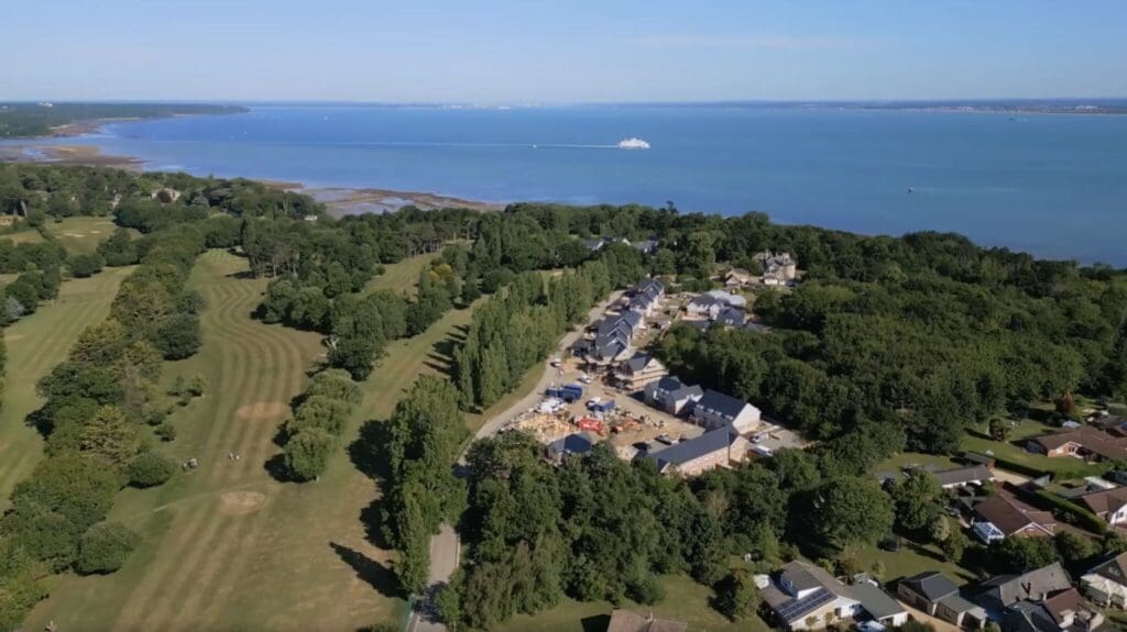 Aerial view of an Isle of Wight timber frame construction site next to a lush golf course and calm blue sea.