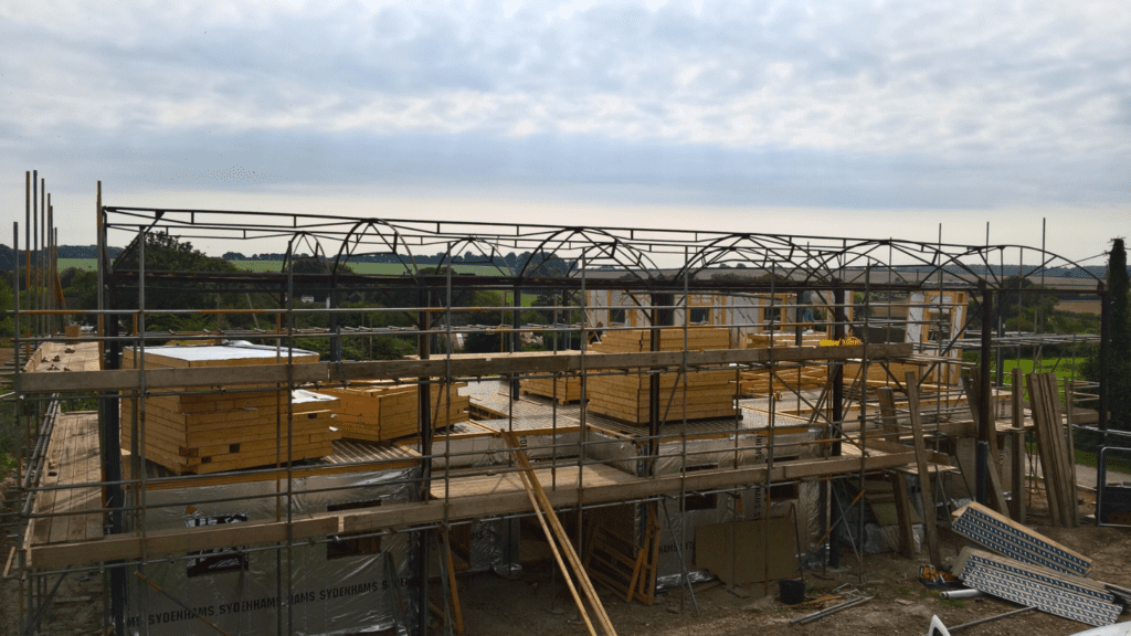 Construction site with scaffolding and stacks of structural timber planks for a Winchester timber frame barn conversion.